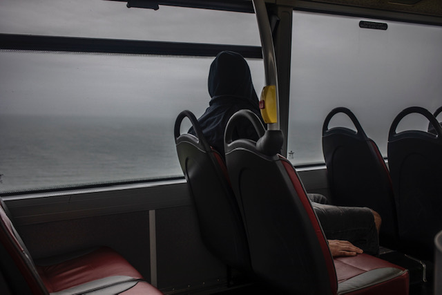 Isolation - images ©Jason Florio - man sits on the the top deck of a bus, overlooking the sea, Cornwall, UK