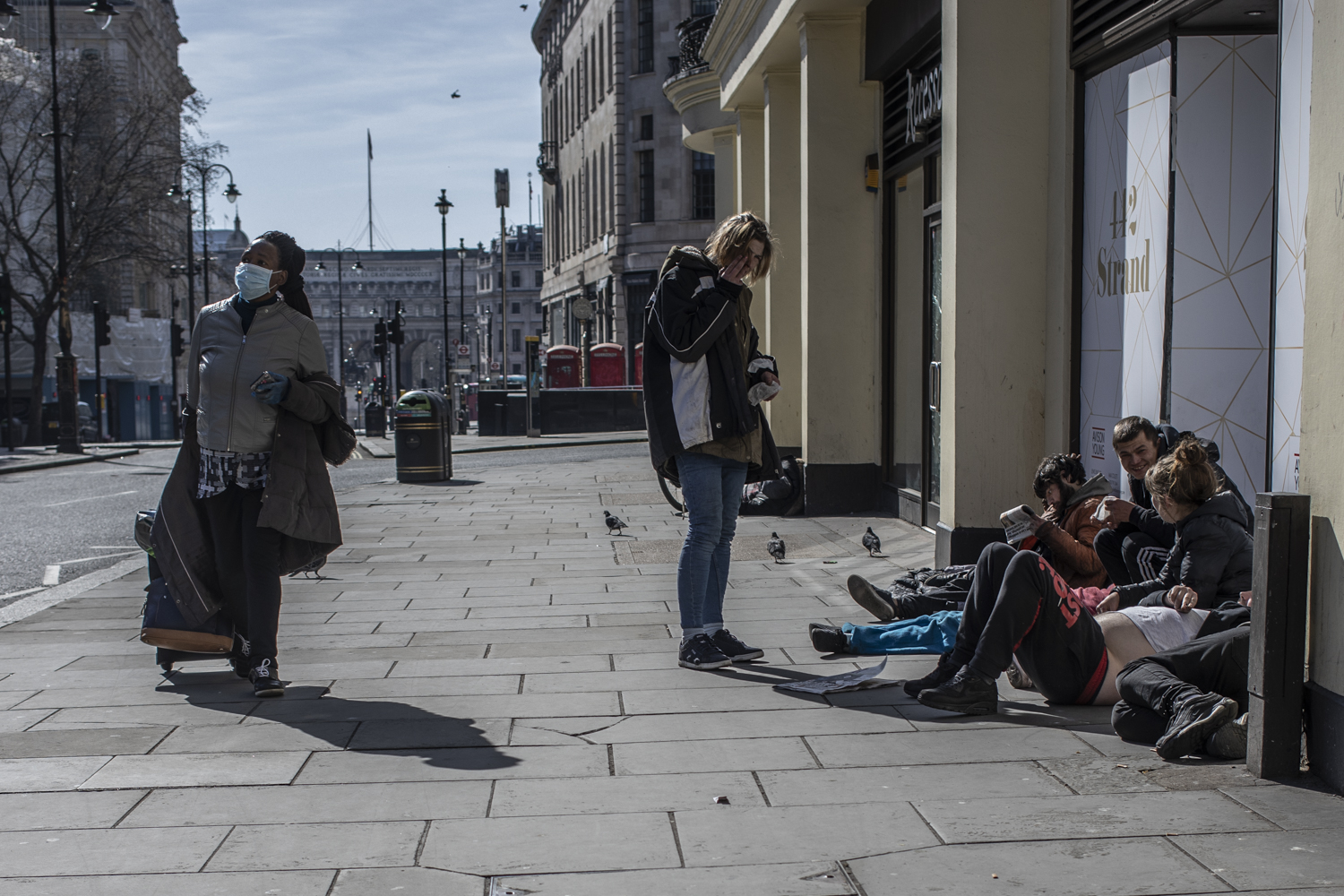 COVID 19 London lockdown. Homelessness - A woman an wearing a face mask walks past a group of homeless people, in a semi-deserted London street ©Jason Florio