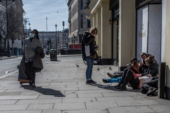 COVID 19 London lockdown. Homelessness - A woman an wearing a face mask walks past a group of homeless people, in a semi-deserted London street ©Jason Florio