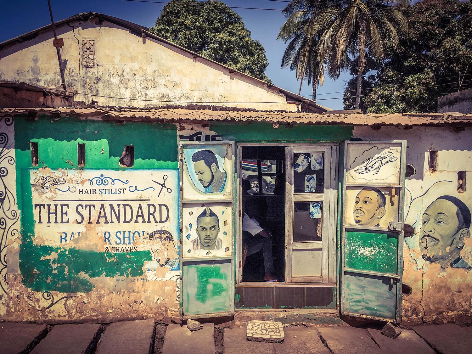 #GambiaDoors: Doors and Storefronts of The Gambia, West Africa - barber shop storefront showing hand-painted hairstyles. Image © Helen Jones-Florio