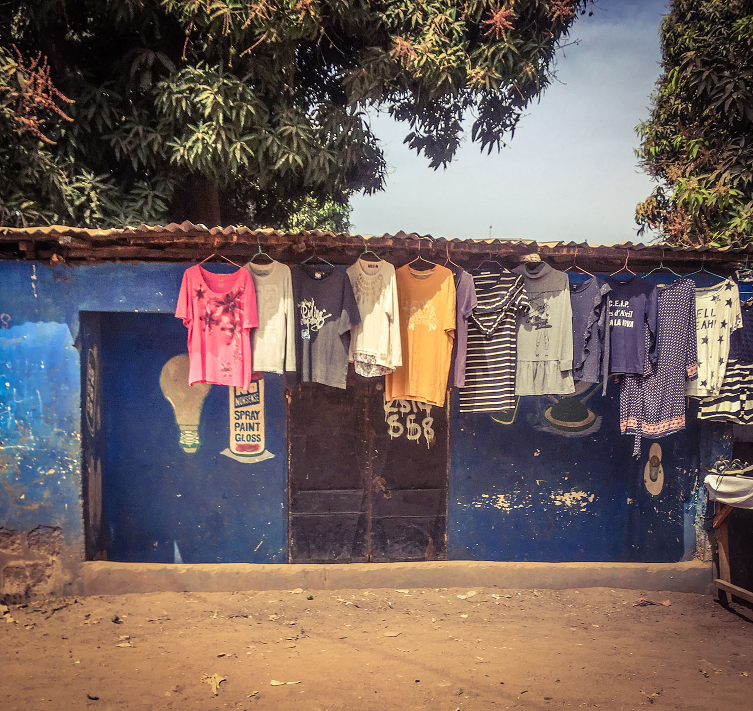 #GambiaDoors: Doors & Storefronts - The Gambia, West Africa. Secondhand clothes hanging outside a shop, Kairaba Avenue. Image ©Helen Jones-Florio