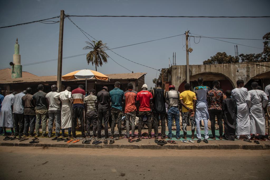 RAMADAN PRAYERS ON THE SIDE OF THE ROADDocumenting Gambia - a line of muslim men doing Friday prayers on the side of an urban road, The Gambia, West Africa. Image ©Jason Florio