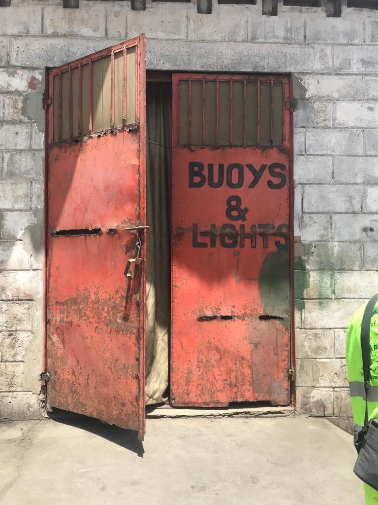 #GambiaDoors - a red metal double door, stands ajar, with the words 'Buoys & Lights', Gambia Port Authority, Banjul The Gambia. Image ©Helen Jones-Florio