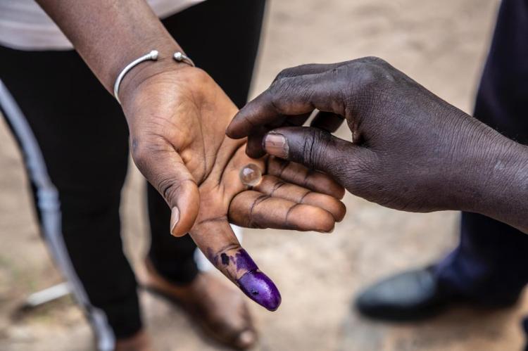 Gambia Elections 2021 - a woman's hand holding marble to vote with, a purple ink finger signifies that the person has voted. Image © Jason Florio