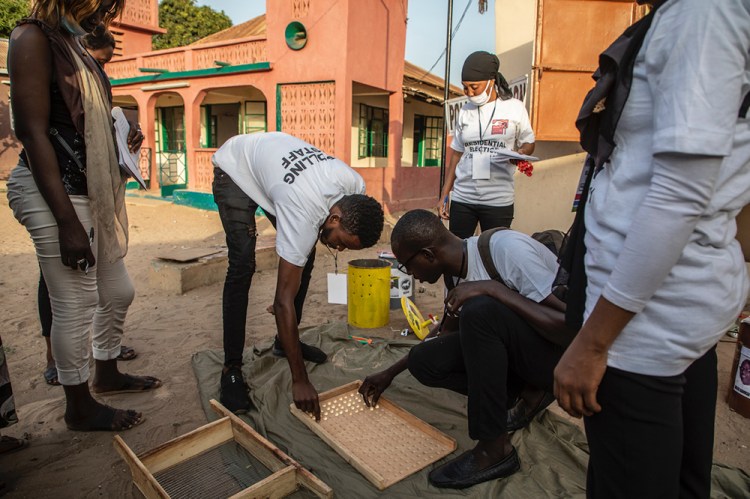 Gambia Elections 2021 - polling staff counting the marble votes, with a mosque in the background. Image © Jason Florio