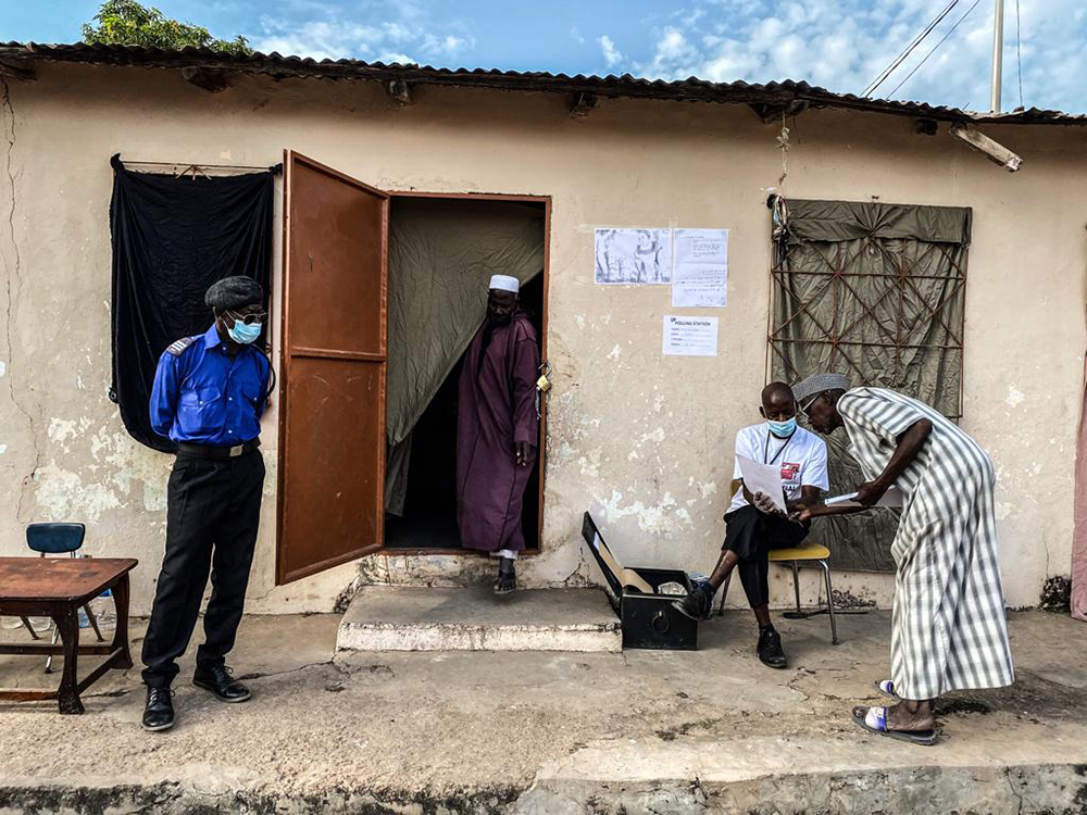 Gambia Elections 2021 -a man emerges from the voting room, guarded by a policeman. Image © Jason Florio