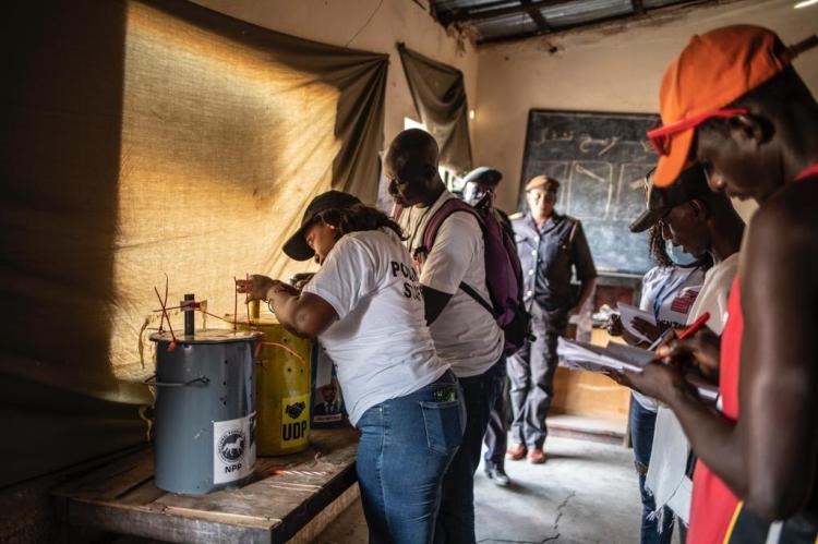 Gambia Elections 2021 -polling staff sealing the voting barrels, containing the voting marbles, as observers make notes. Image © Jason Florio