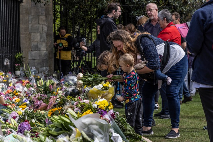 On the day following the announcement of the death of Queen Elizabeth of the United Kingdom, a young boy lays a bouquet of flowers at the gate of Windsor Castle. People have flowcked to Windsor to leave flowers and pay their respects. Image © Jason Florio