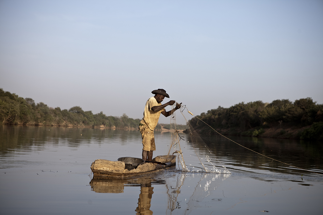 A fisherman standing in a dug out canoe, pulling up his nets, on the River Gambia, The Gambia. Image ©Jason Florio